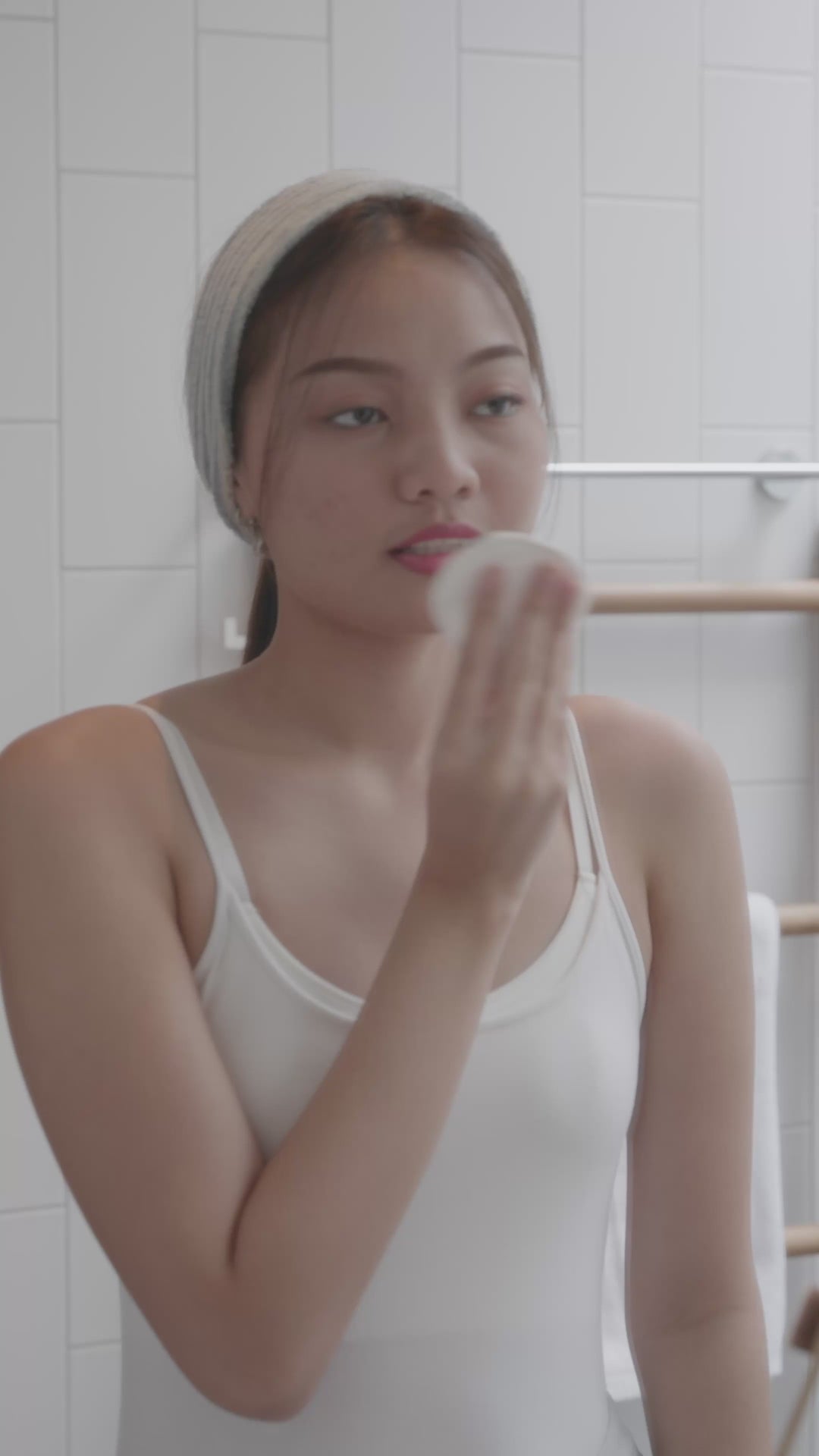 Une femme passe un coton sur son visage dans la salle de bain